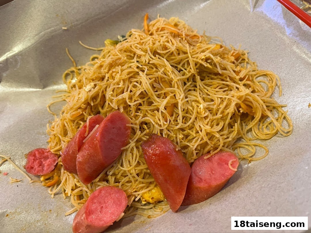 A close-up of stir-fried vermicelli noodles served with sliced sausages on a paper-lined plate.