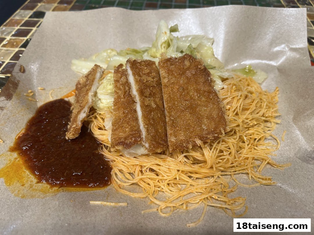 A close-up of crispy fried cutlets served with thin noodles, cabbage, and a rich sauce on paper.