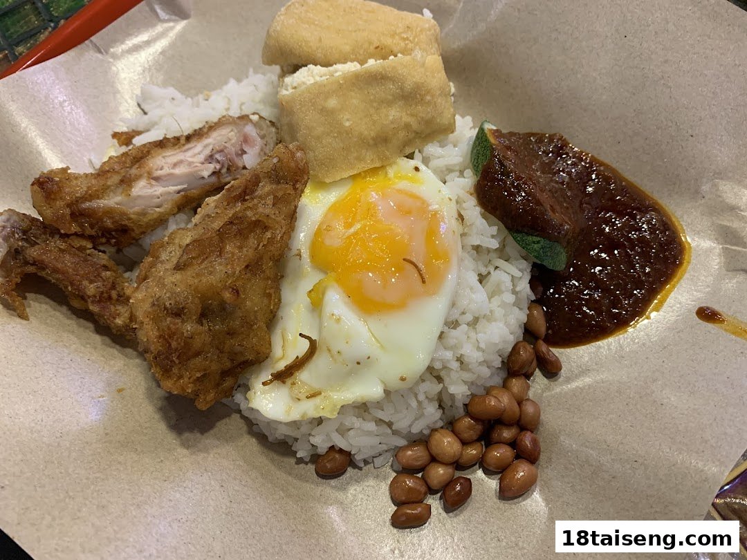 A delicious plate of Nasi Lemak with fried chicken, egg, peanuts, and sambal, served on paper.