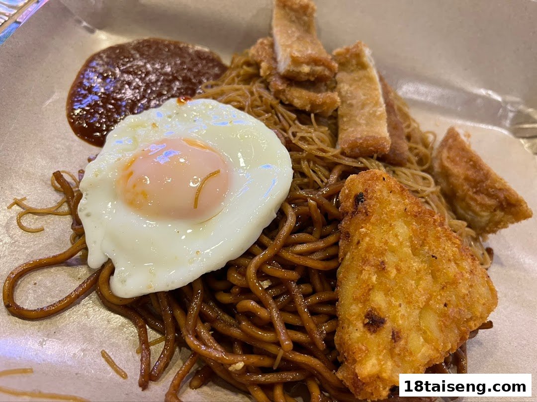A delicious plate of dark sauce noodles topped with a fried egg, chili sauce, and crispy fried items.