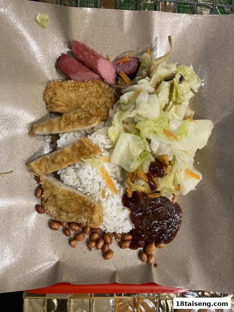 A delicious meal featuring rice, fried chicken, sausages, vegetables, and peanuts, served on paper.