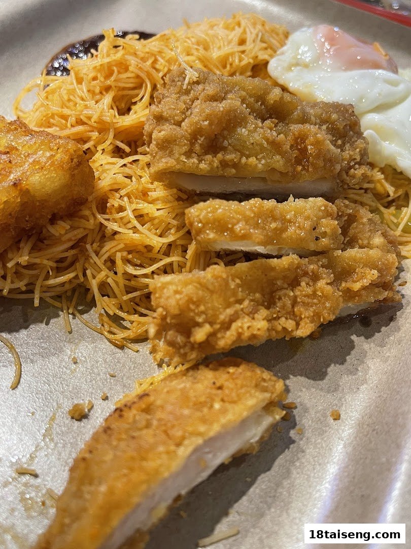 A close-up of crispy fried chicken served with vermicelli noodles, a fried egg, and sauce.