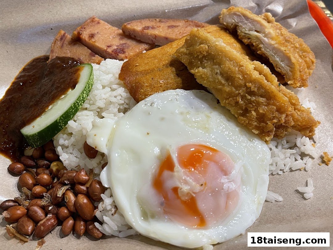A close-up of a delicious Nasi Lemak dish with fried chicken, egg, peanuts, and sambal.