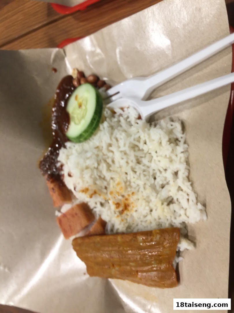 A close-up of a Nasi Lemak dish with rice, sambal, cucumber, and various toppings.