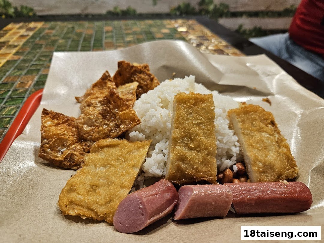 A close-up of a meal featuring white rice, fried items, and sausages served on brown paper.