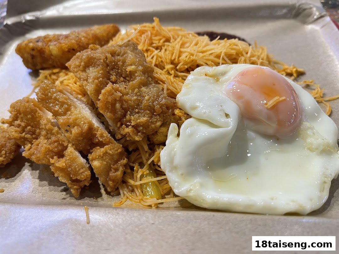 A close-up of a meal featuring fried chicken, noodles, a fried egg, and a spring roll.