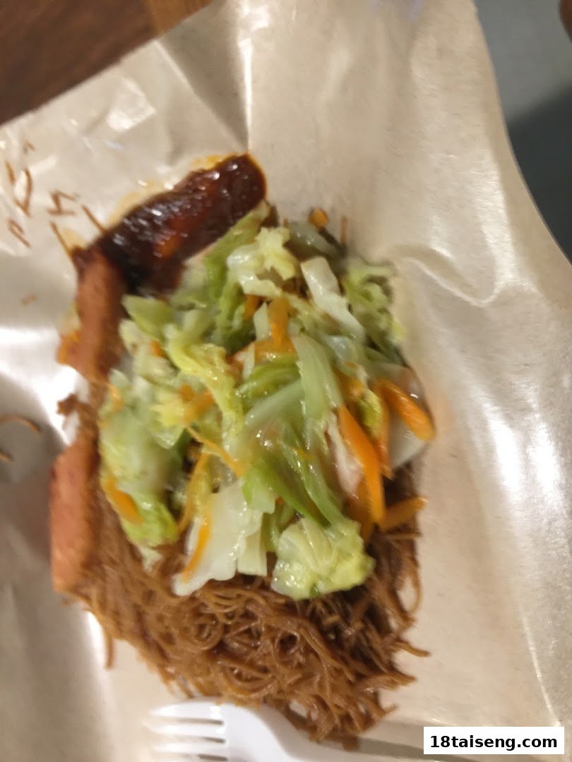 A close-up of a delicious noodle dish with vegetables and sausage, served in paper packaging.