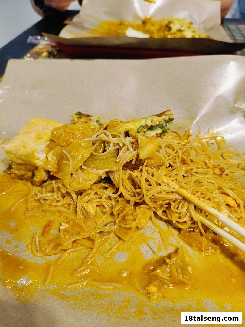A close-up of delicious noodles with a rich, yellow curry-like sauce, served on paper.