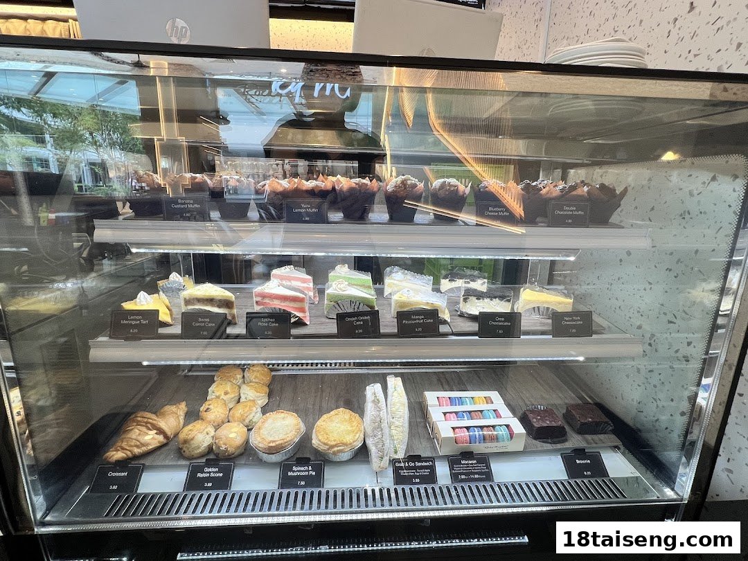 A glass display case showcasing a variety of freshly baked muffins, cakes, pastries, and desserts.