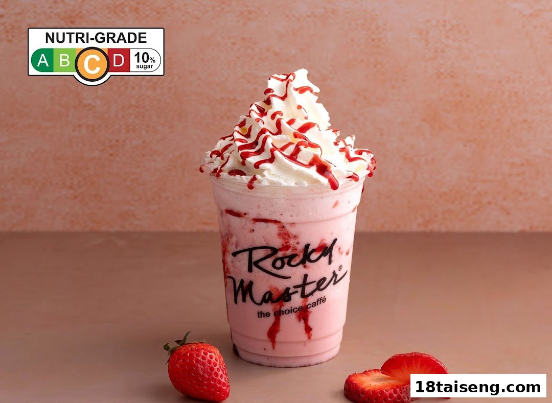 A vibrant strawberry milkshake from Rocky Master, topped with whipped cream and strawberry drizzle, with fresh strawberries.