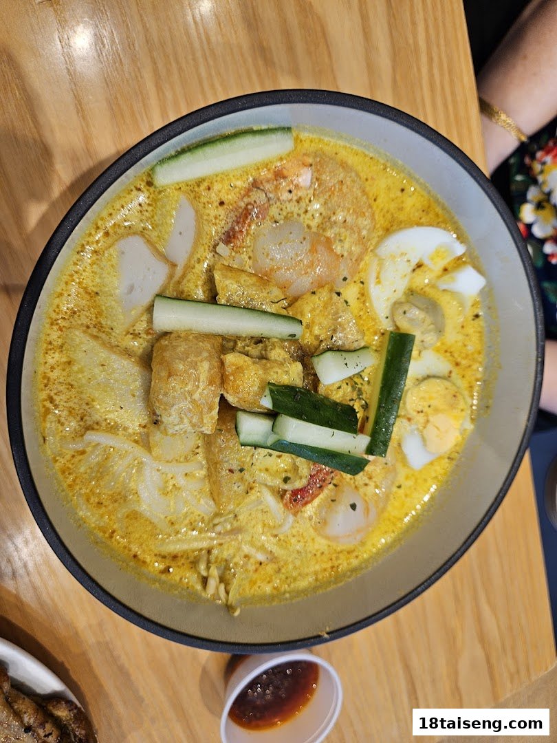 A vibrant bowl of laksa with prawns, fish cake, egg, and cucumber on a wooden table.