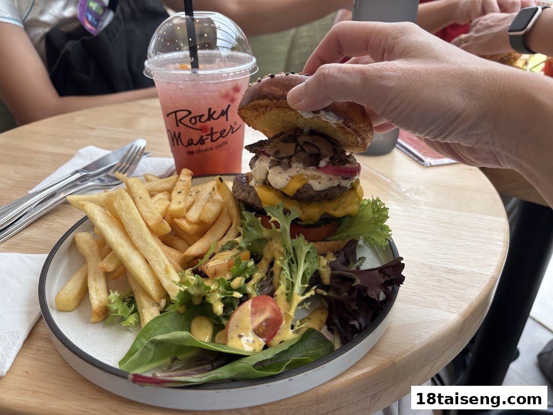 A gourmet burger with fries and salad, alongside a refreshing drink, served on a wooden table.