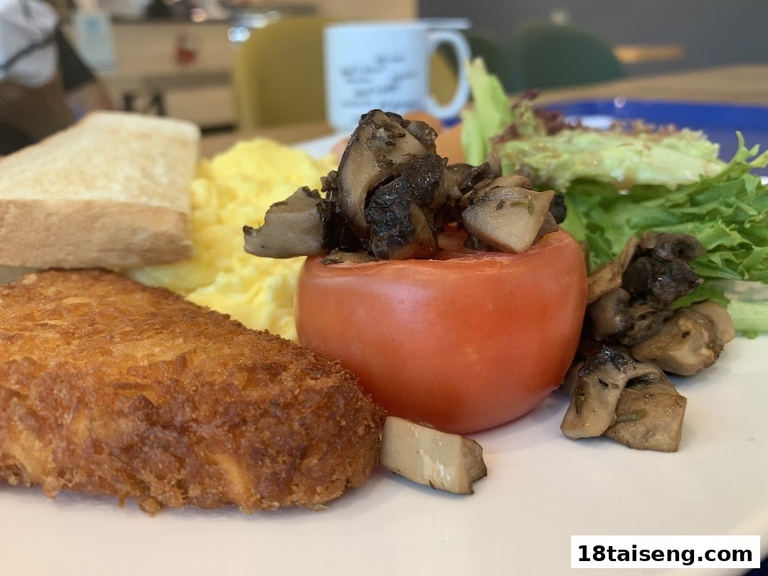 A delicious breakfast plate featuring hash brown, scrambled eggs, toast, roasted tomato with mushrooms, and fresh salad.