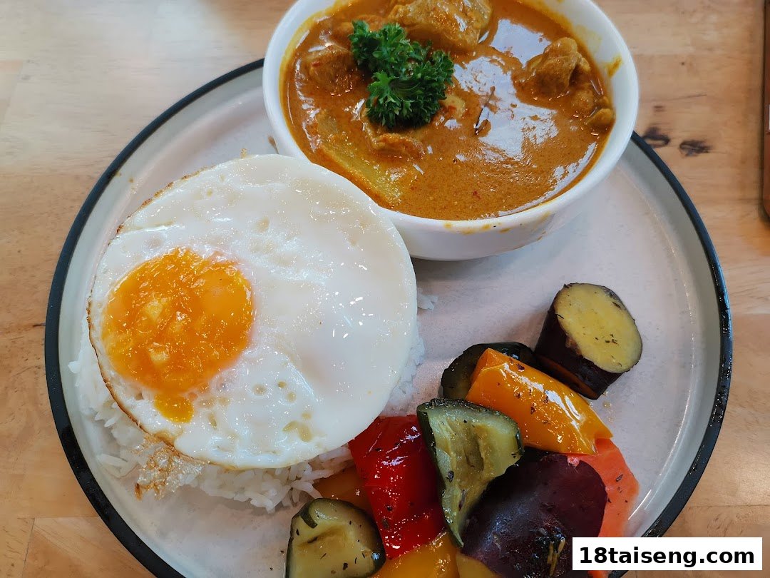 A delicious meal featuring chicken curry, rice, a sunny-side-up egg, and roasted vegetables on a plate.