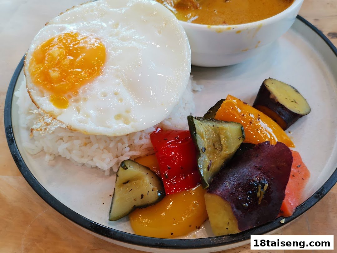 A plate of rice with a fried egg, roasted vegetables, and a bowl of curry.