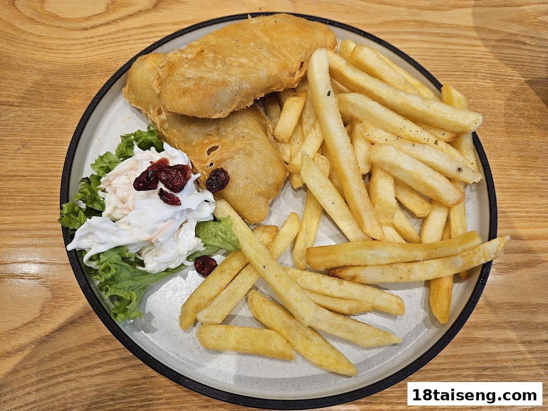 A plate of golden-brown fish and chips served with fresh coleslaw and cranberries on a wooden table.