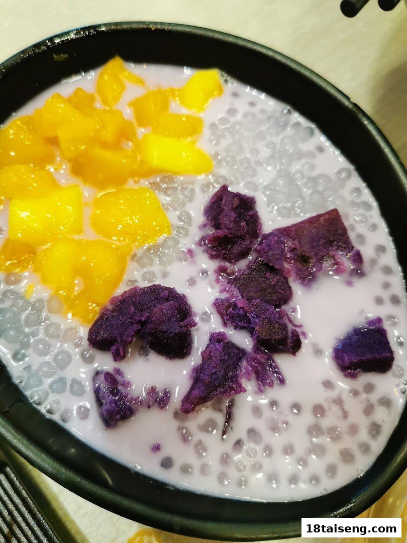 A vibrant bowl of Thai dessert with mango, purple yam, and sago pearls in coconut milk.