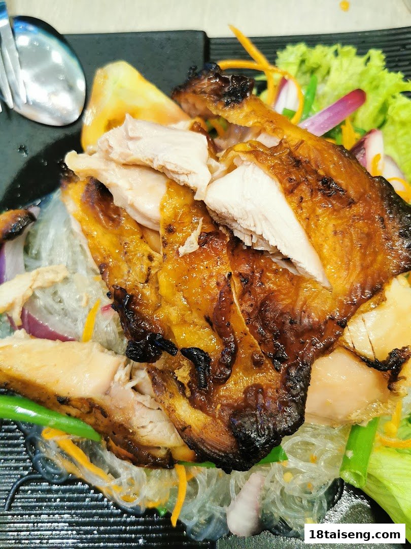A close-up of grilled chicken served with glass noodles and fresh vegetables.