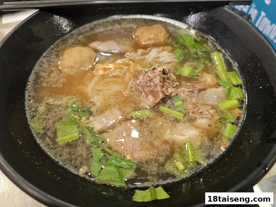 A close-up of a hearty bowl of Thai boat noodles with meat, meatballs, and greens.