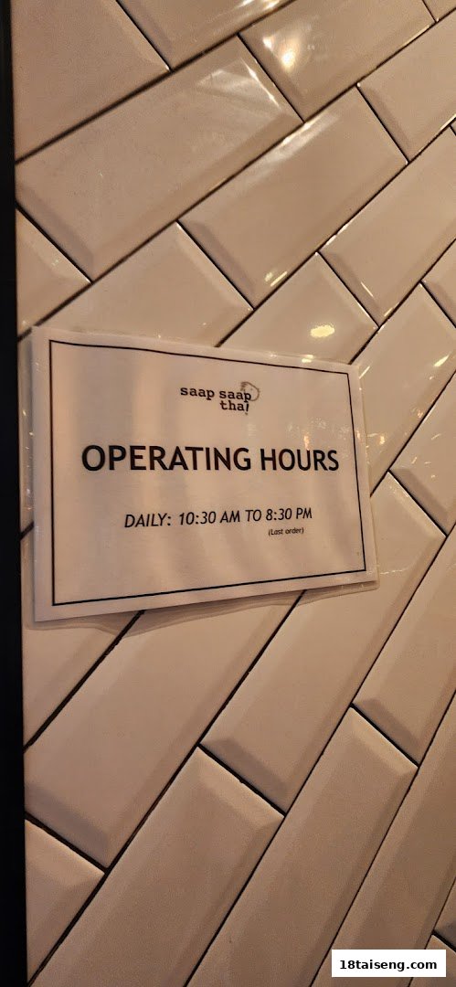 A sign displaying Saap Saap Thai's daily operating hours on a tiled wall.