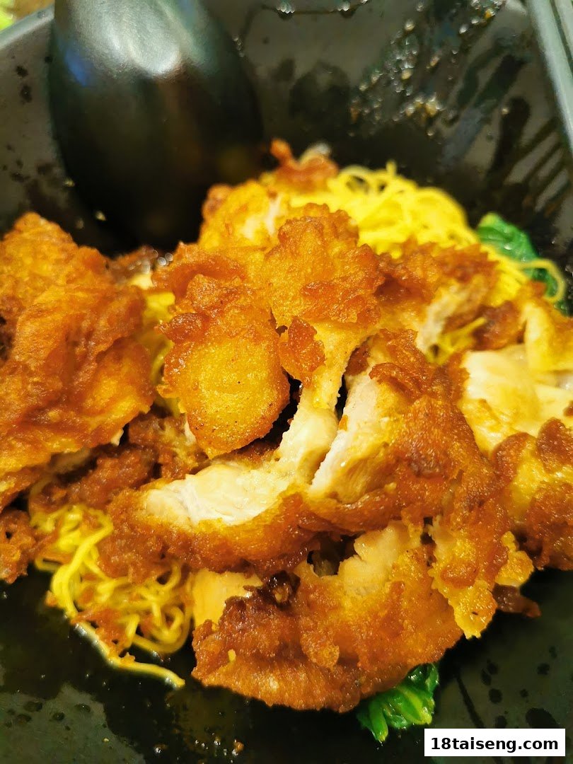 A close-up of crispy fried chicken served over yellow noodles with greens.