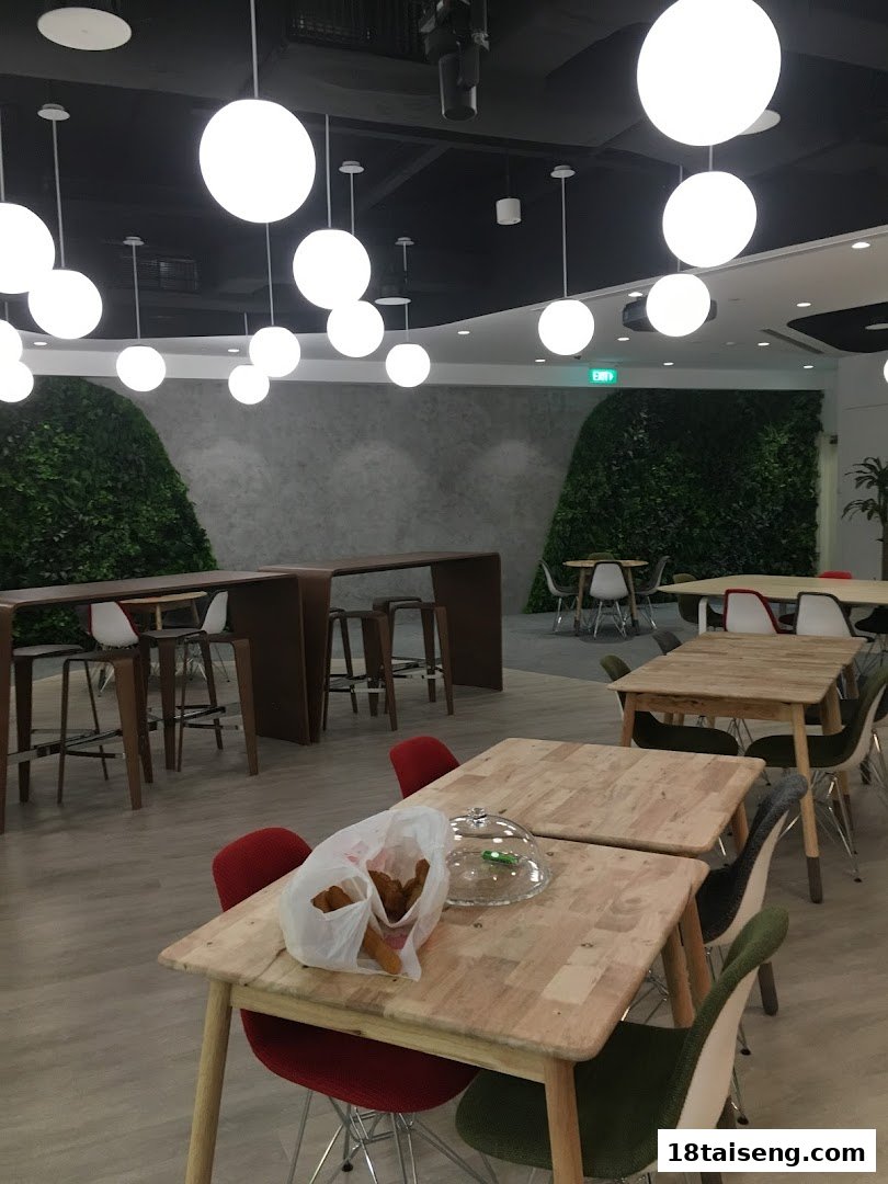 A modern, spacious cafeteria or breakout area with various seating options and green wall accents.