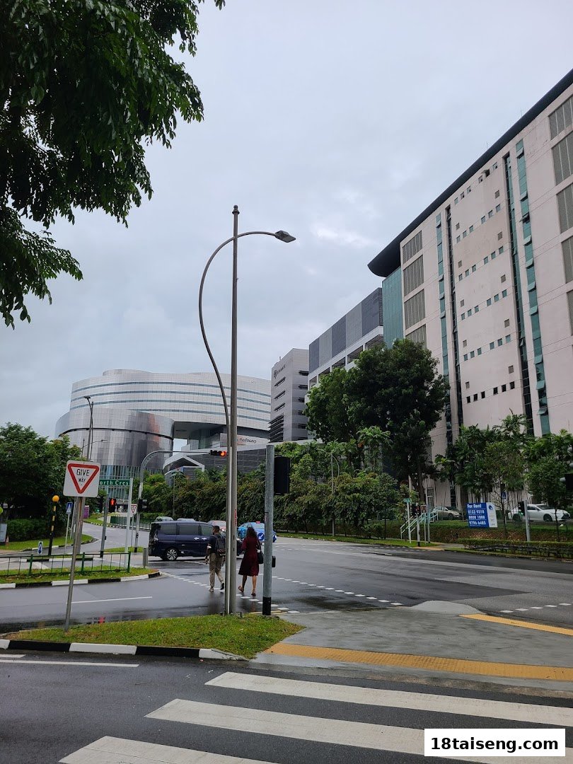 A street intersection with modern buildings, pedestrians, and vehicles under a cloudy sky.
