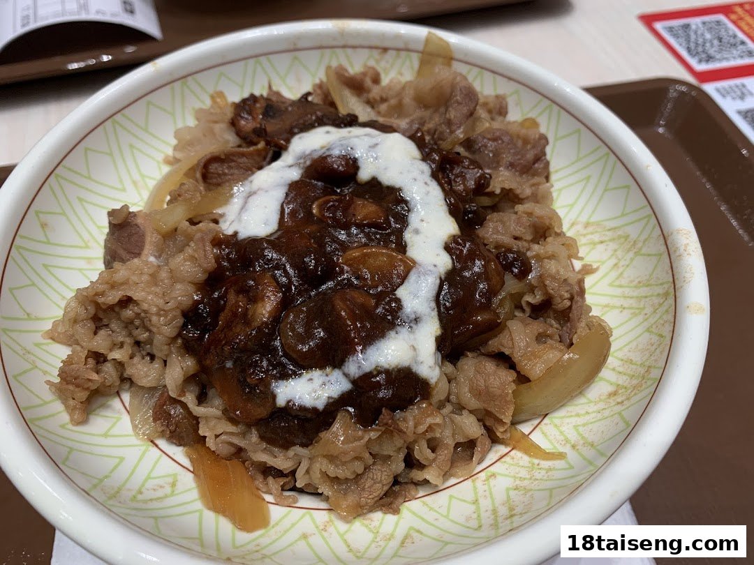 A close-up of a Sukiya gyudon bowl topped with beef, onions, a rich sauce, and a creamy drizzle.