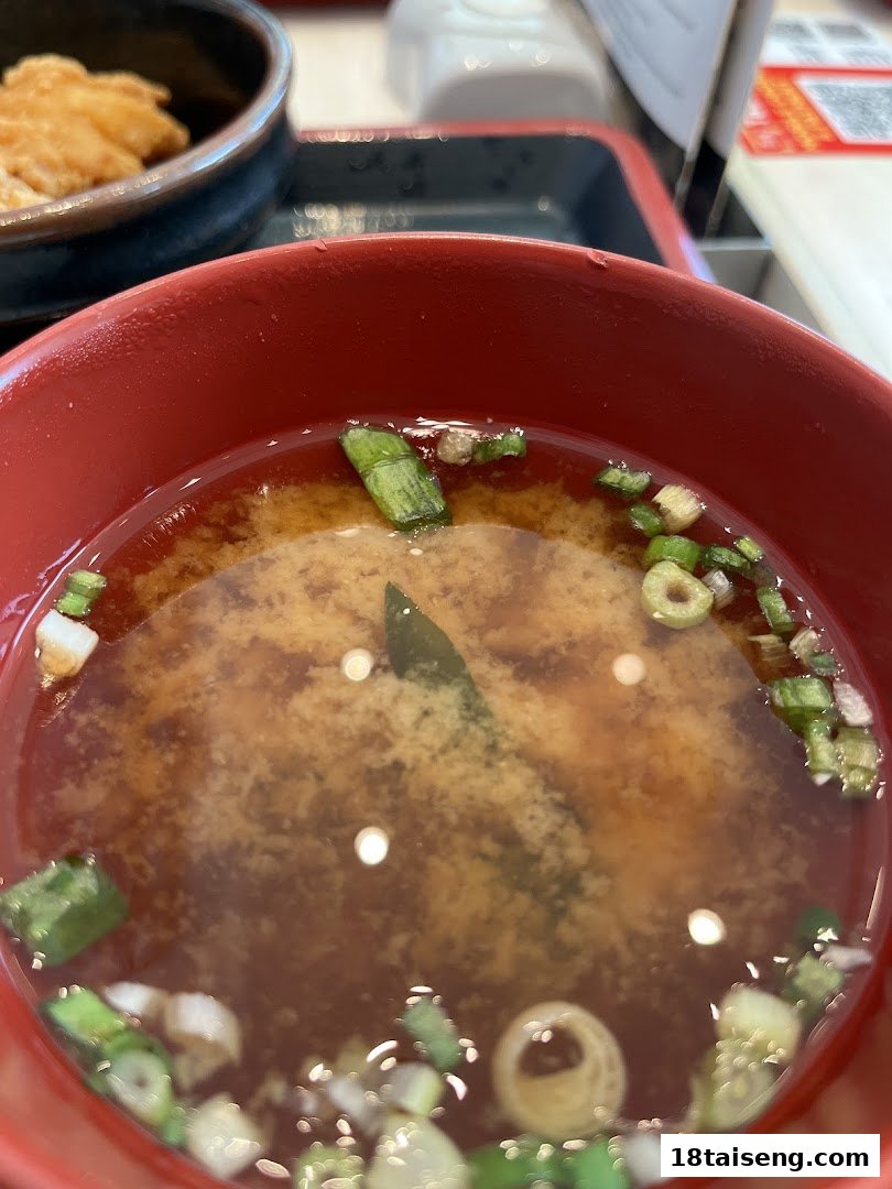 A close-up of a red bowl filled with miso soup, garnished with green onions and seaweed.