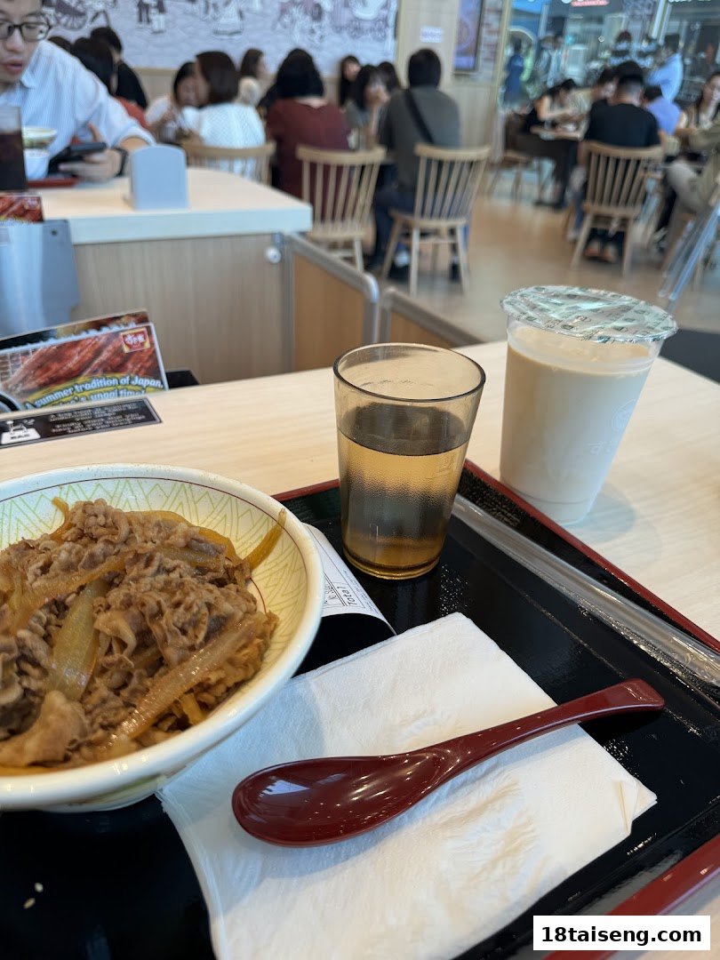 A bowl of gyudon, drinks, and diners enjoying a meal at Sukiya.