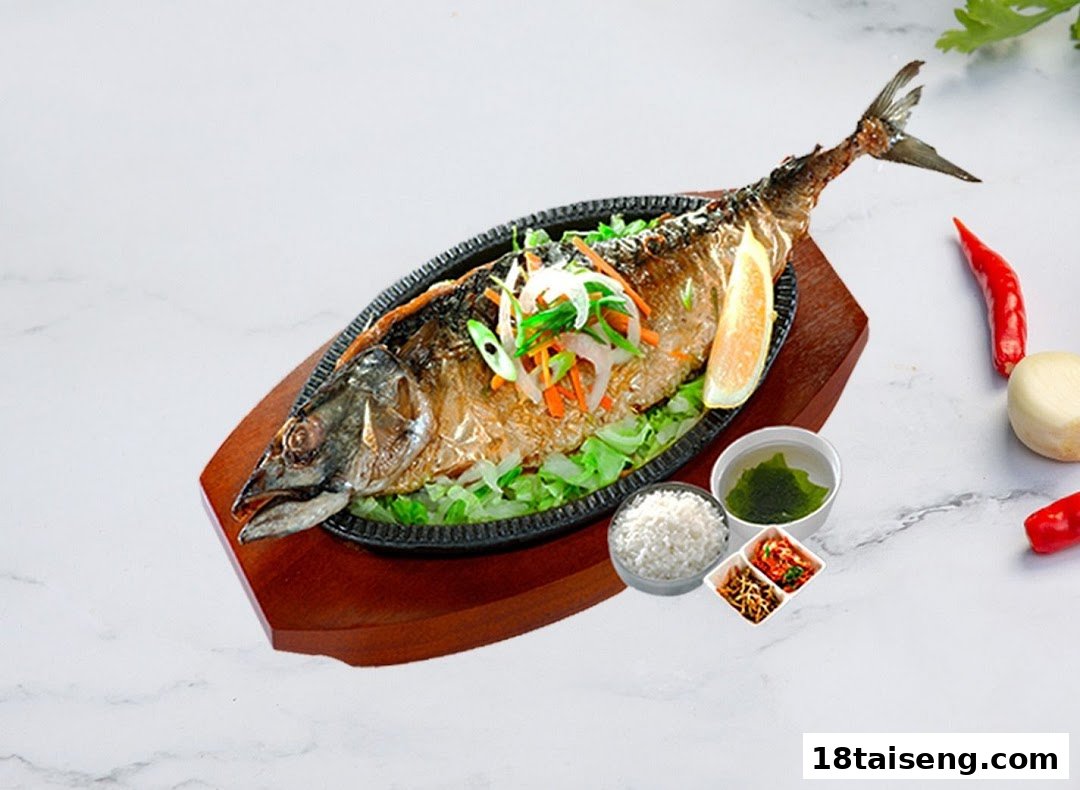 A sizzling grilled fish dish with rice, soup, and banchan, garnished with lemon and vegetables.