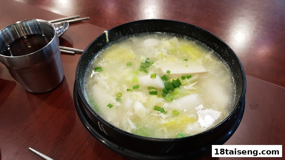 A comforting bowl of Korean soup with rice cakes, tofu, and green onions, served on a wooden table.