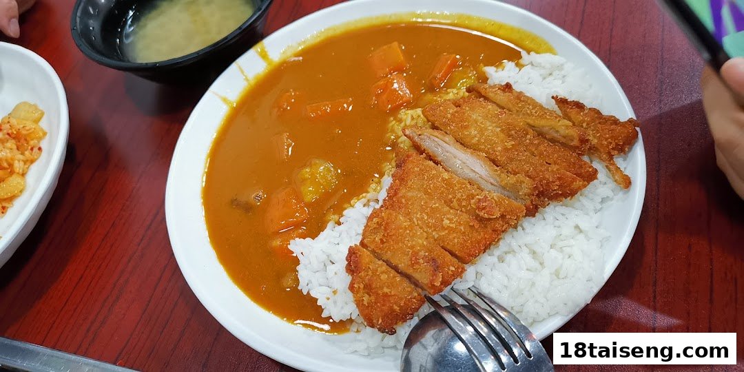 A delicious plate of golden curry with crispy katsu and white rice, served with side dishes.