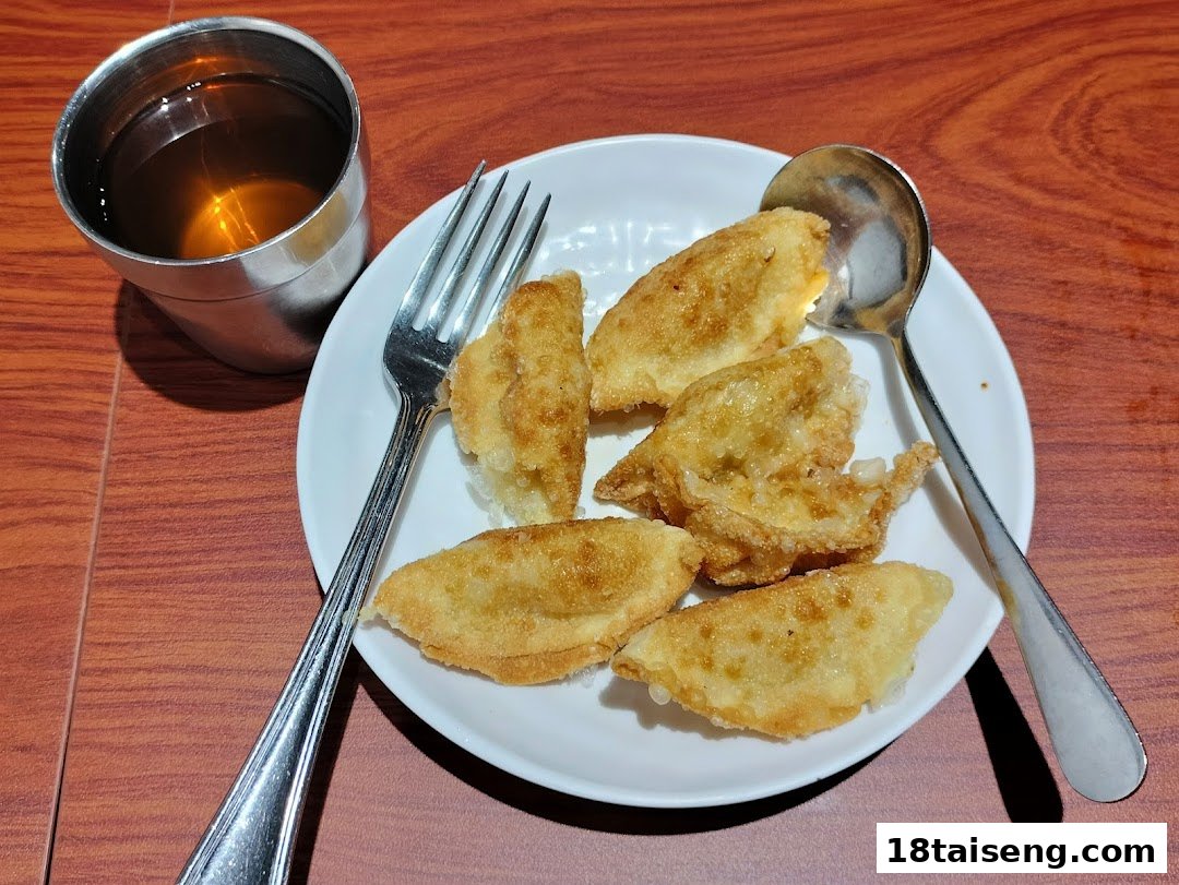 A plate of golden-fried Korean dumplings with a metal cup of tea on a wooden table.