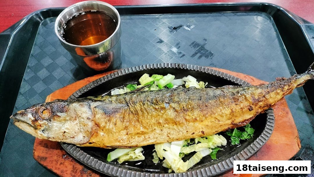 A whole grilled fish served on a sizzling plate with vegetables and a drink at Sunny Korean.