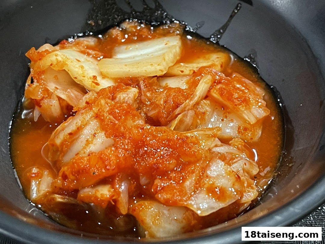 A close-up of vibrant red kimchi, a traditional Korean side dish, in a black bowl.