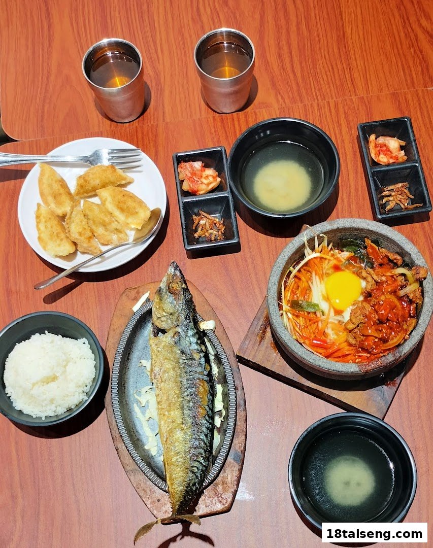 A table set with a Korean meal featuring grilled fish, bibimbap, dumplings, rice, and banchan.