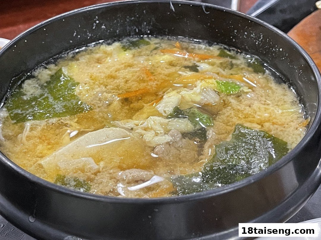 A close-up of a hearty Korean soup or stew, featuring meat, vegetables, and egg in a rich broth.
