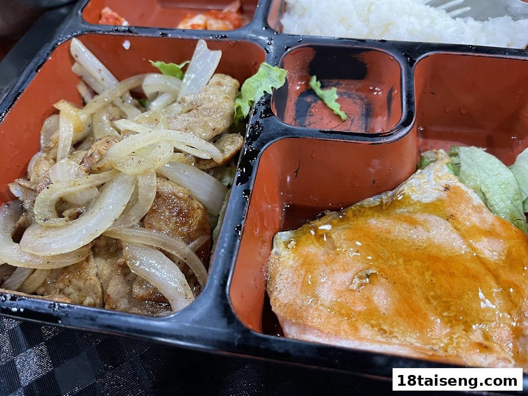 A close-up of a delicious Korean bento box featuring glazed salmon, stir-fried meat with onions, and rice.