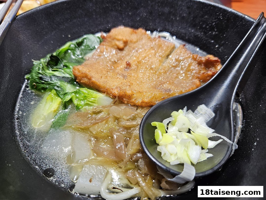A close-up of a delicious bowl of Taiwanese noodles with a fried cutlet, vegetables, and scallions.