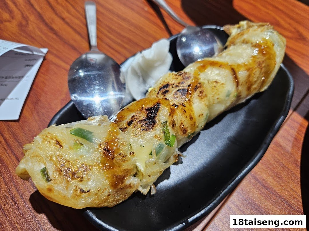 A delicious Taiwanese scallion pancake roll, drizzled with sauce, served on a black plate.