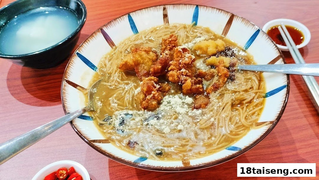 A close-up of a delicious bowl of Taiwanese vermicelli with crispy fried chicken, soup, and condiments.
