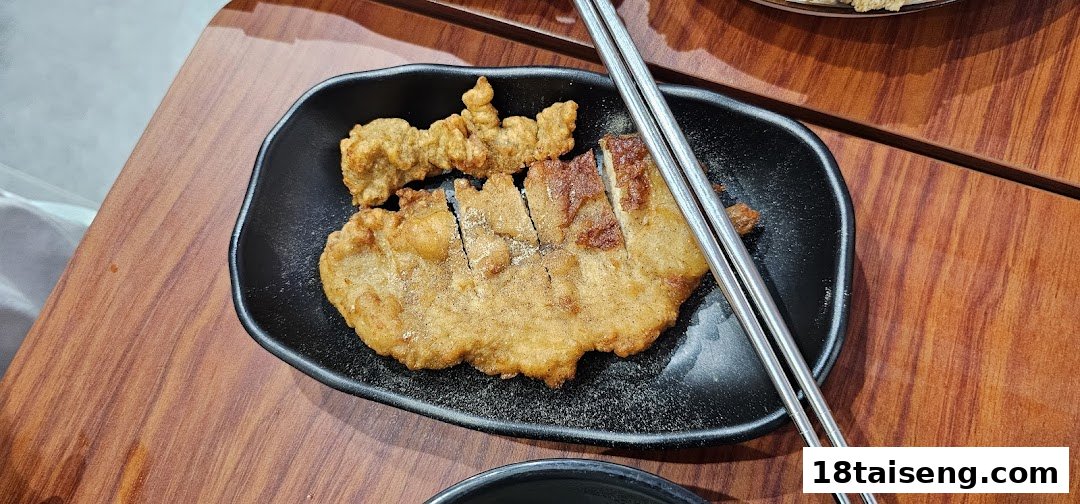 A black plate featuring a golden-brown fried pork chop and another fried item, with chopsticks resting on the side.