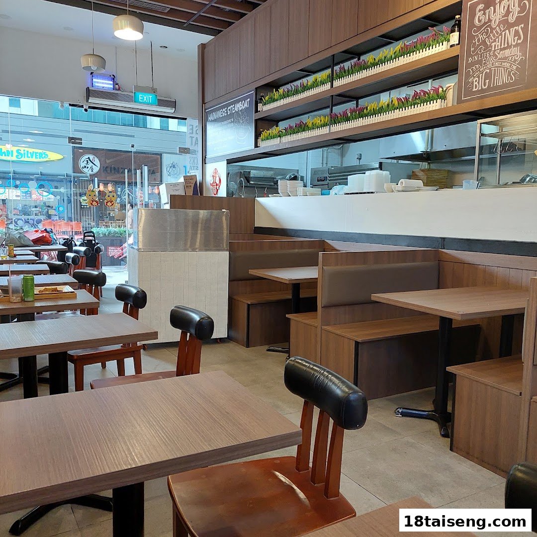 Interior view of The Hainan Colony restaurant featuring wooden tables, booth seating, and a serving counter.