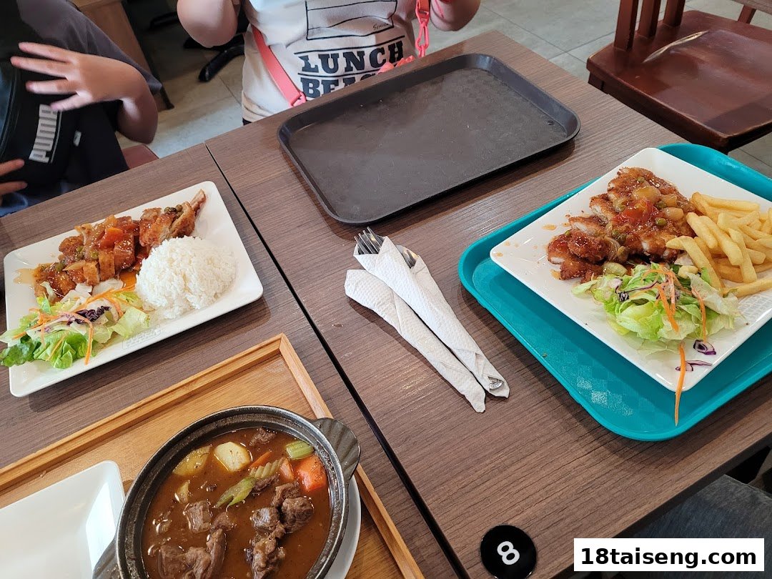A table with various Hainanese dishes, including fried chicken with rice, fries, and a hearty stew, ready to be enjoyed.