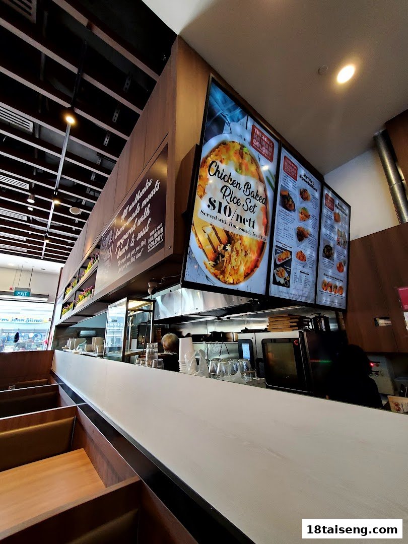 Interior view of The Hainan Colony, featuring comfortable seating, a service counter, and digital menu displays.
