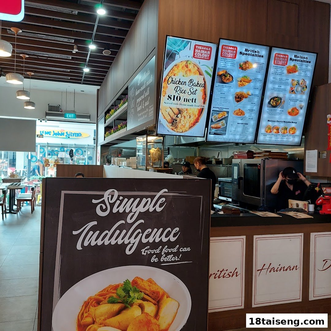 An interior view of The Hainan Colony restaurant, featuring digital menu boards, a service counter, and a promotional standee.