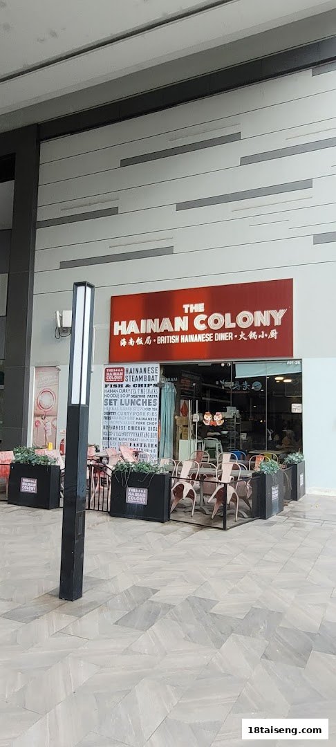 The exterior of The Hainan Colony, a British Hainanese diner, featuring outdoor seating and a prominent red sign.