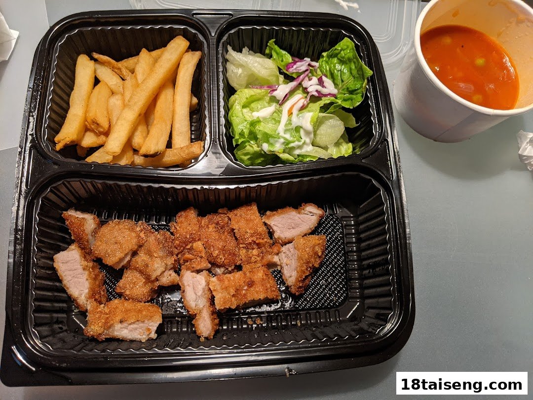 A delicious Hainanese takeout meal featuring crispy fried pork, golden fries, fresh salad, and a side of soup.