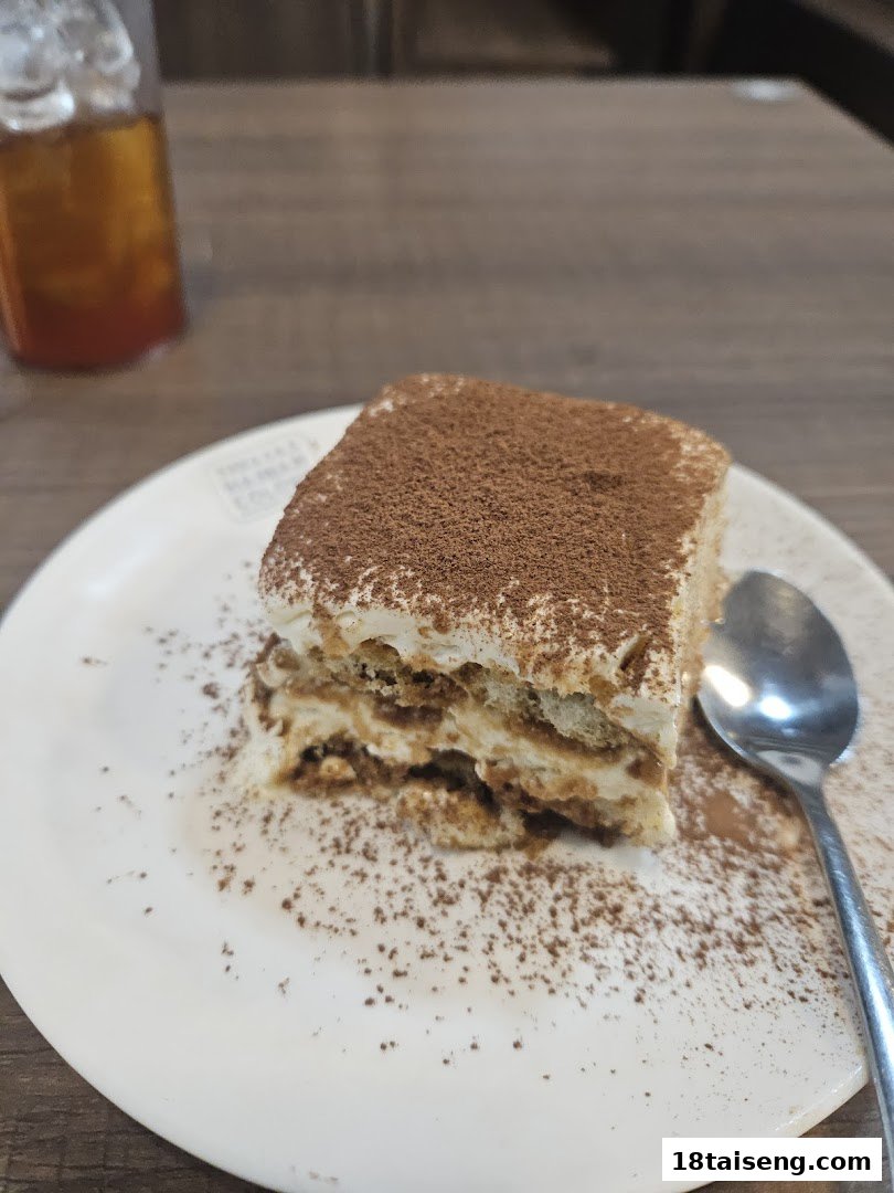 A delectable slice of tiramisu, generously dusted with cocoa powder, served on a white plate.